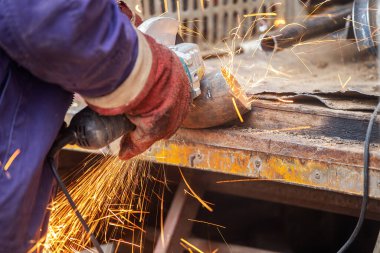 Çalışan bir adam üretim, fabrika fiziksel işçiliği, bir adam bir Bulgar tutuyor, metal bir diskle demir bir boru kesiyor, kıvılcımlar uçuşuyor, tehlikeli işler yapıyor.