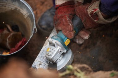 Çalışan bir adam üretim, fabrika fiziksel işçiliği, bir adam bir Bulgar tutuyor, metal bir diskle demir bir boru kesiyor, kıvılcımlar uçuşuyor, tehlikeli işler yapıyor.