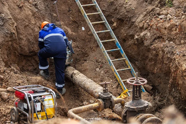 Üniformalı bir adam gaz borusunu tamir etmekle, ekipmanları aletlerle tamir etmekle, demir iletişim tamirciliğiyle, onların durumunu iyileştirmekle ve insanların güvenliğini sağlamakla meşgul.