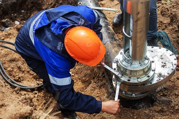 Üniformalı bir adam gaz borusunu tamir etmekle, ekipmanları aletlerle tamir etmekle, demir iletişim tamirciliğiyle, onların durumunu iyileştirmekle ve insanların güvenliğini sağlamakla meşgul.