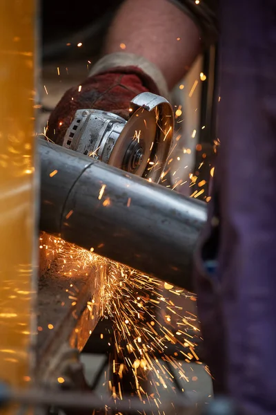 a man in working form is working on production, factory physical labor, a man is holding a Bulgarian, he is sawing an iron pipe with a metal disk, sparks are flying, dangerous work