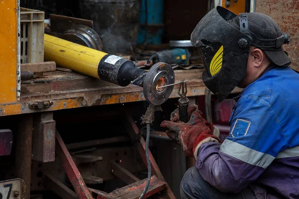 a man in a welder\'s mask and in a robe works in the factory, is engaged in welding work, the flow of hot plasma welds the seam on a metal pipe, production, plant and rough work
