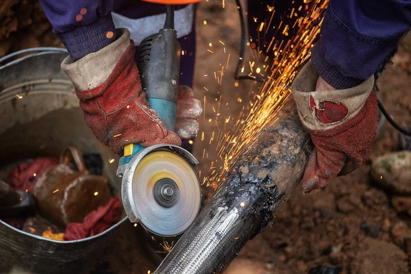 a man in working form is working on production, factory physical labor, a man is holding a Bulgarian, he is sawing an iron pipe with a metal disk, sparks are flying, dangerous work