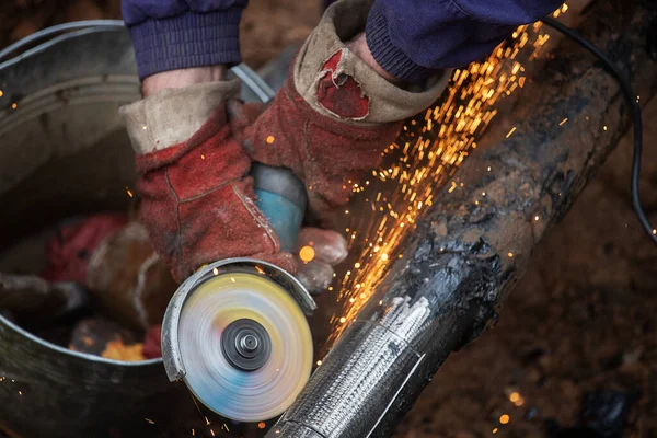 Çalışan bir adam üretim, fabrika fiziksel işçiliği, bir adam bir Bulgar tutuyor, metal bir diskle demir bir boru kesiyor, kıvılcımlar uçuşuyor, tehlikeli işler yapıyor.
