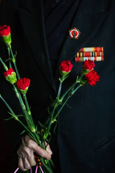 Yaşlı bir savaş gazisinin elleri çiçekleri tutuyor. Kırmızı karanfiller, İkinci Dünya Savaşı 'nı kazananların anısına askeri bayram hediyesi. Vatansever bayram zafer günü. Tebrikler yaşlı adam.