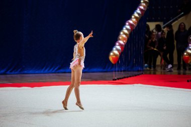 Bir kız artistik jimnastikçi bir yarışmada egzersiz yapıyor. Çevik sporcu güzel bir şekilde tek ayak üzerinde duruyor.