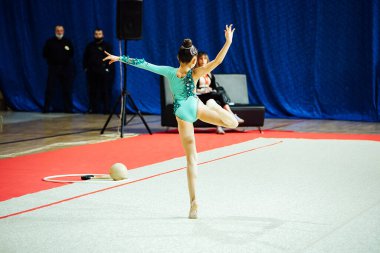 Bir kız artistik jimnastikçi bir yarışmada egzersiz yapıyor. Çevik sporcu güzel bir şekilde tek ayak üzerinde duruyor.
