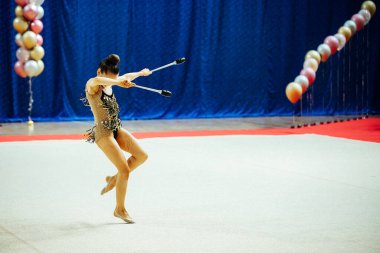 Bir kız artistik jimnastikçi bir yarışmada egzersiz yapıyor. Çevik sporcu güzel bir şekilde tek ayak üzerinde duruyor.