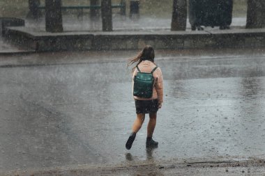 Islak bir kız yağmurda şemsiyesiz yürür. Islak saçlar, elbiseler ve soğuk bir rüzgar. Şehirdeki kötü hava. Yayalar ıslak ayaklarıyla su birikintilerinde yürür.