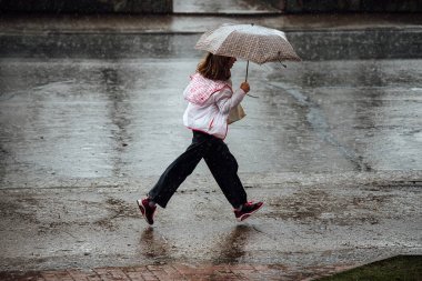 Şemsiyeli bir kız yağmurda su birikintilerinde koşar. Şiddetli bir yağmurda ıslak ayaklar ve giysiler. Bir adam havadan kaçar.