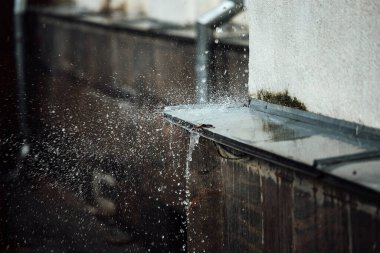 Düşen yağmur damlaları çıkıntıda kırılır. Akan sudan fışkırıyor. Bir yağmur fırtınası sırasında binanın çatısından drenaj borusu.