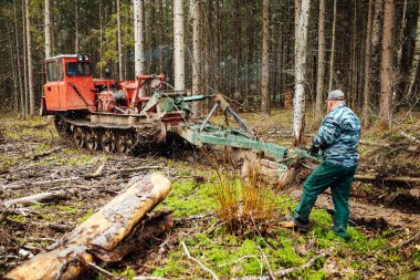 Bir sürüngen traktörü bir orman açıklığından geçiyor. Endüstriyel buldozer çamura saplanmış. Kamyonlar yerde kayıyor.