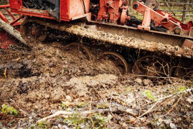 Bir sürüngen traktörü bir orman açıklığından geçiyor. Endüstriyel buldozer çamura saplanmış. Kamyonlar yerde kayıyor.