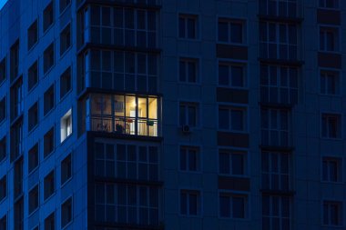 Çok katlı bir apartmanın çok katlı penceresinin birinde ışık yanıyor.