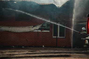 Bir kurtarma ekibi evdeki yangını söndürdü. İtfaiyeciler alevlerin üzerine su döker. Yanan binadan duman ve sis