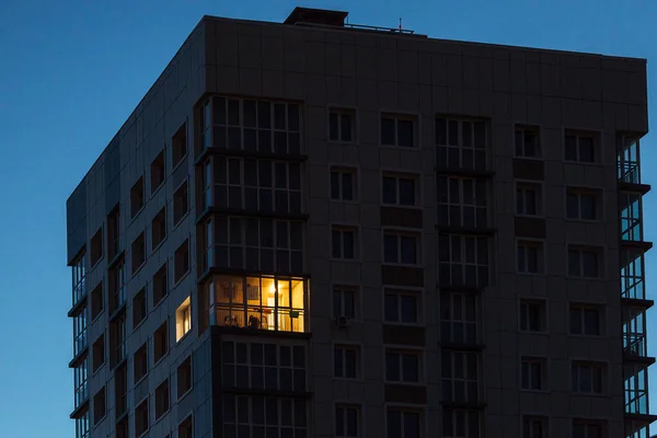 Çok katlı bir apartmanın çok katlı penceresinin birinde ışık yanıyor.
