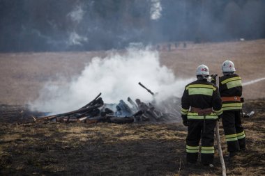 İtfaiyeciler küllerin üzerinde. Yangını söndürme işini tamamladım. Yanan evdeki yanmış odun parçalarının incelenmesi. Sis ve yanık kokusu.