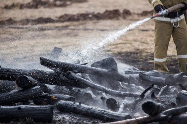 İtfaiyeciler küllerin üzerinde. Yangını söndürme işini tamamladım. Yanan evdeki yanmış odun parçalarının incelenmesi. Sis ve yanık kokusu.