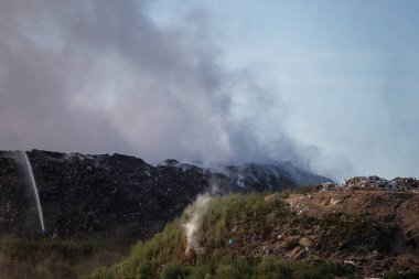 Çöp sahasında yangın. Yanan plastikten kaynaklanan zehirli atık bulutu. Çöp sahasında çıkan yangından kaynaklanan zararlı emisyonlar. Çöp yanıkları ve dumanlar metan gazı üretiyor. Çöp sahasındaki yangını söndürmek
