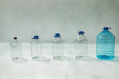 Beyaz arka planda farklı boyutlarda birkaç boş plastik şişe duruyor. Sıvılar için tek kullanımlık konteynırlar. Plastikten yapılmış farklı şişe ve konserve çeşitleri