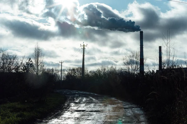 the pipes of the thermal power plant smoke on the horizon. country autumn landscape. withering nature and environmental pollution. technical pond for cooling the factory furnace