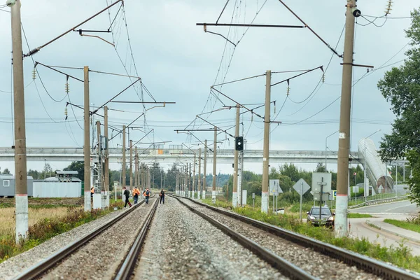 workers in orange uniforms walk along the railway tracks. the repair team is going to work by rail. stone embankment of the railway and power lines. it is dangerous to walk on railway tracks