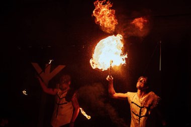 Efsanevi bir yaratığın maskesi içindeki bir ateş sanatçısı ateşle gösteri yapıyor. Sokak kültürü festivali. Geceleri renkli mistik ateş gösterisi