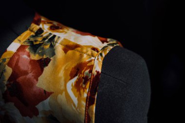 Bir mankenin üzerinde el yapımı parlak bir elbise. Moda tasarımcısı bireysel terzilikten bir elbise yapar. Çiçek desenli kumaş. Siyah arka planda bir mankenin üzerindeki kıyafetlerin fotoğrafı.