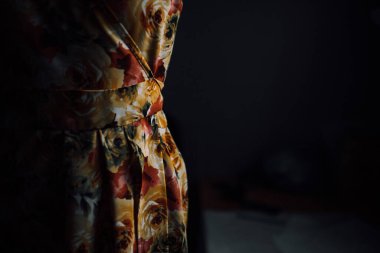 Bir mankenin üzerinde el yapımı parlak bir elbise. Moda tasarımcısı bireysel terzilikten bir elbise yapar. Çiçek desenli kumaş. Siyah arka planda bir mankenin üzerindeki kıyafetlerin fotoğrafı.