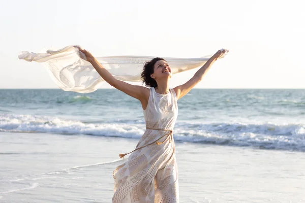 하얀 드레스를 입은 한 아름다운 소녀가 손에 파레 오를 들고 해변을 따라 걸어 다닌다 — 스톡 사진
