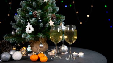 Yeni yılın durgun hayatı, Noel ağacının arka planındaki masada iki bardak şampanya mandalinası. siyah arkaplan