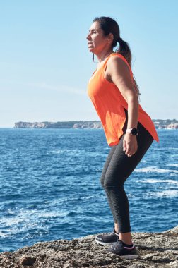 Latin kadın, orta yaşlı, spor giyer, spor giyer, antrenman yapar, fiziksel egzersiz yapar, kalas, mekik, tırmanış basamağı, kalori yakar, formda kalır, deniz kenarında, kulaklık takar, akıllı saat takar.