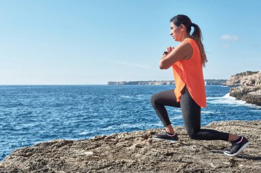 Latin kadın, orta yaşlı, spor giyer, spor giyer, antrenman yapar, fiziksel egzersiz yapar, kalas, mekik, tırmanış basamağı, kalori yakar, formda kalır, deniz kenarında, kulaklık takar, akıllı saat takar.