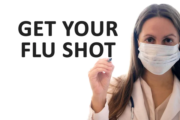 Доктор женщина в маске держит ручку и пишет получить прививку от гриппа текст — стоковое фото