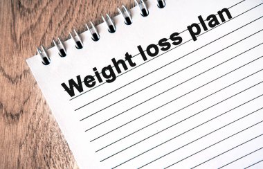 Kilo verme planı: Ahşap bir masanın üzerinde çizgileri olan beyaz bir defter üzerindeki siyah metin.