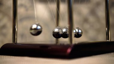 Newtons Beşiği, iş sembolü. Metal toplardan sarkaç.