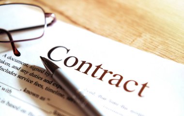 Gözlüklü sözleşme kağıdı ve tahta arka planda bir kalem.