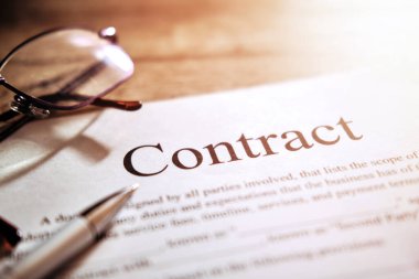 Gözlüklü sözleşme kağıdı ve tahta arka planda bir kalem.