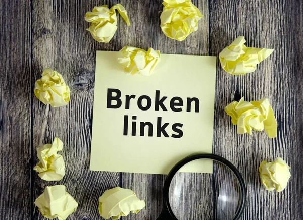 Broken links - text on yellow note sheets on a dark wooden background with crumpled sheets and a magnifying glass