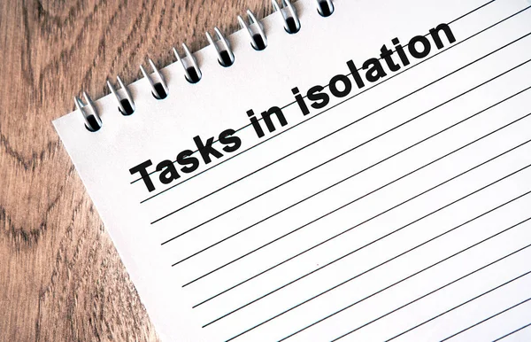 TASKS IN ISOLATION - black text on a white notebook with lines on a wooden table