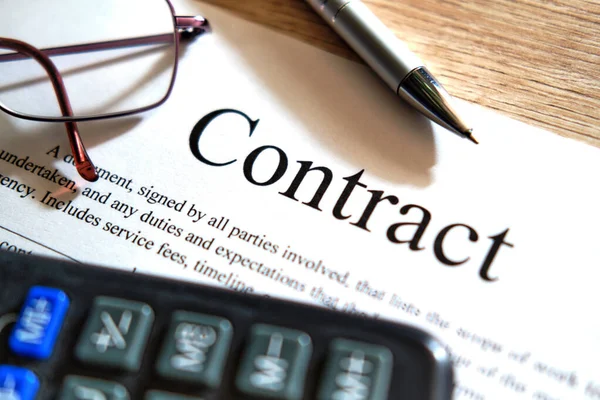 A pen for the signature of the Contract. Glasses and calculator on a black calculator on a wooden table