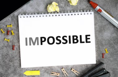 Beton bir masanın üzerinde iğne, işaret ve zımba bulunan beyaz bir defterde imkansız bir metin.