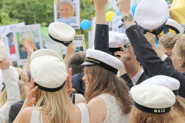 Счастливые подростки, поднимающие шапку выпускника, празднуя граду
