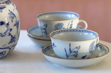 Keten kumaş ve pembe bir duvarın arkasında bir masada beyaz ve mavi porselen kahve seti yapılmış