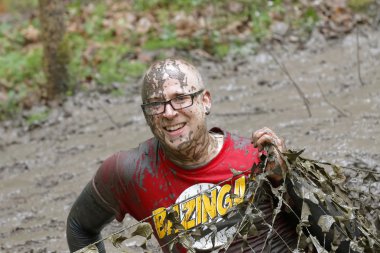 Bir kamuflaj ağı altında sürünen çamur ile kaplı gülümseyen adam