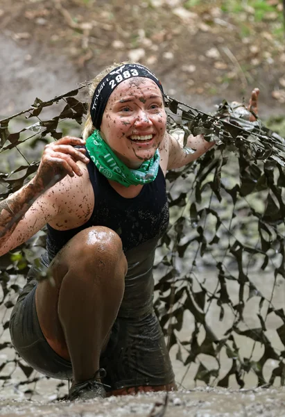 Donna sorridente coperta di fango che striscia sotto una rete di camuffamento — Foto Stock