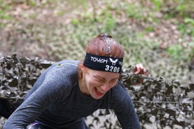 STOCKHOLM, SWEDEN - MAY 14, 2016: Smiling womanwith mud in her hair crawling up from a camouflage net in the obstacle race Tough Viking Event in Sweden, April 14, 2016