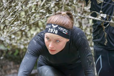 Kamuflaj ağının altında çamurla kaplanmış bir kadın.