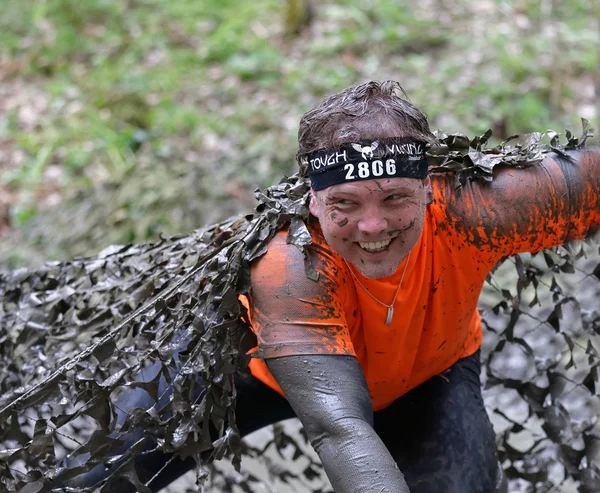 Homme souriant couvert de boue rampant sous un filet de camouflage — Photo