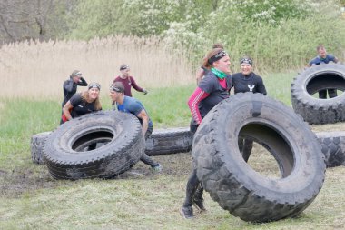 STOCKHOLM, SWEDEN - MAY 14, 2016: Group of men and woman struggling to tip a large tractor tire obstacle in the obstacle race Tough Viking Event in Sweden, April 14, 2016